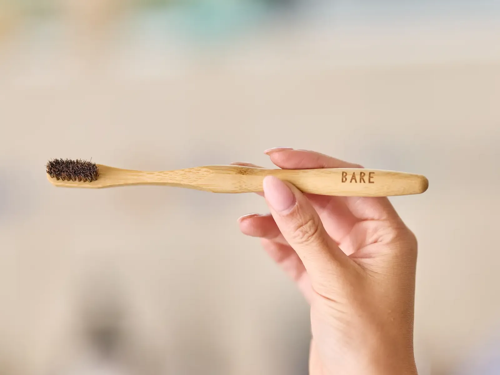 A hand holding the BARE toothbrush level, the BARE engraving on the bamboo handle and the dark horse-hair bristles in focus