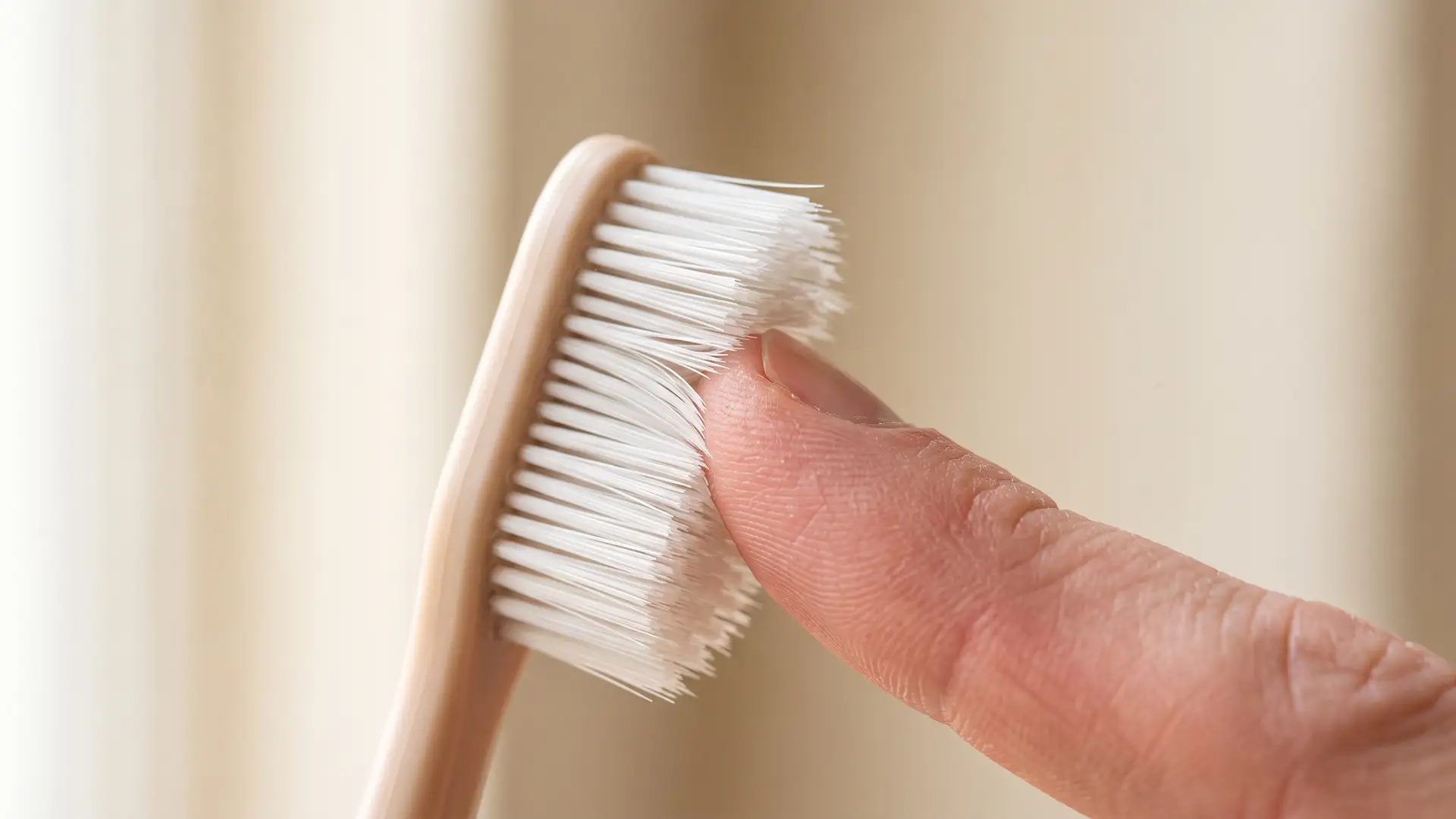 Very fine soft toothbrush bristles flexing gently as they press against a fingertip, showing how easily they bend.