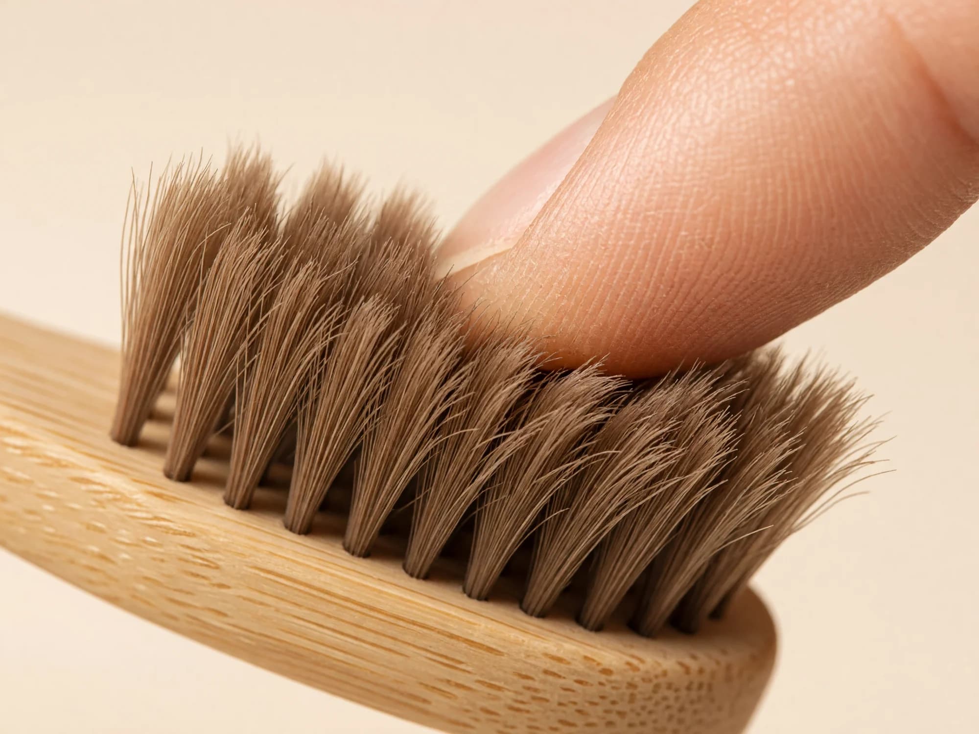 Ultra-fine soft horse-hair toothbrush bristles flexing under a fingertip on a bamboo head, looking plush and gentle.